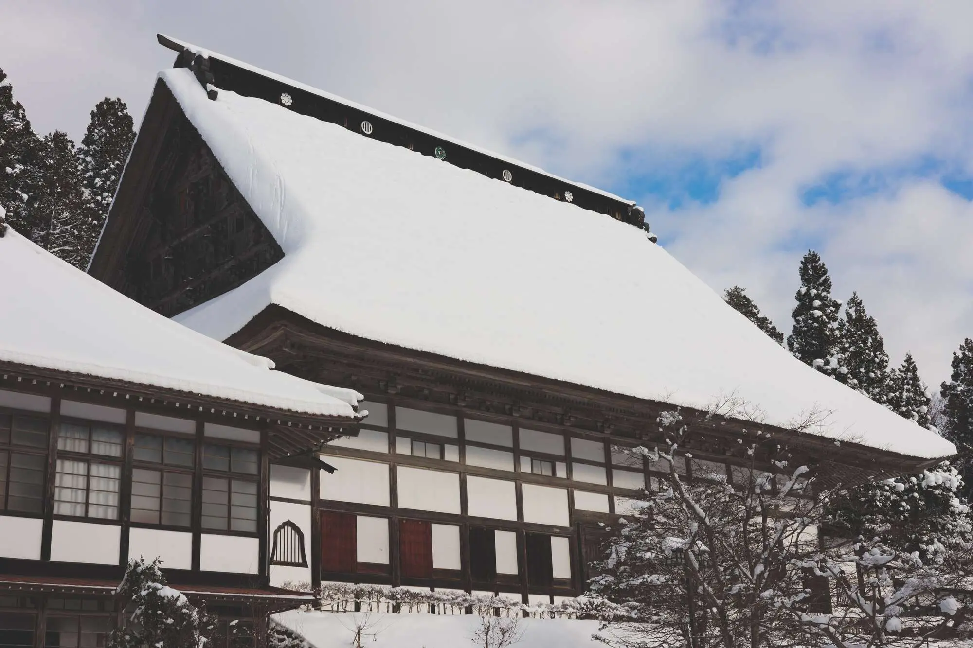 Traditional Japanese building with a snow-covered roof, surrounded by evergreen trees in winter.