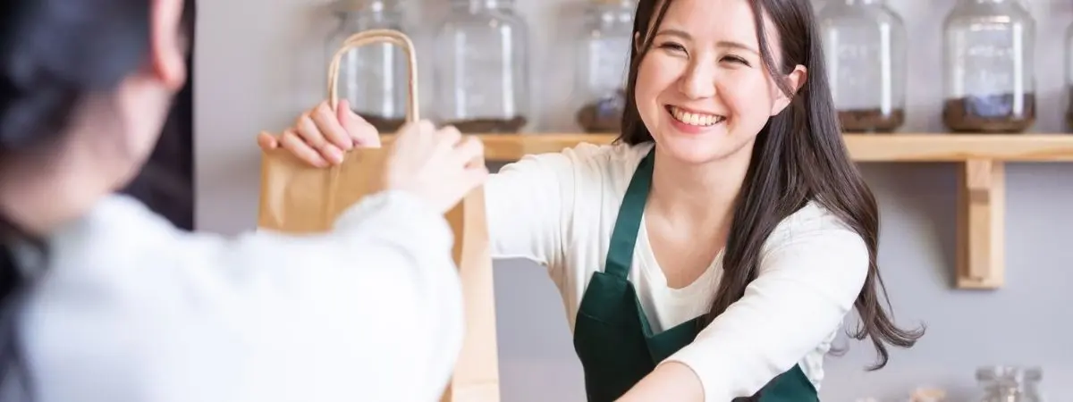 Smiling server hands a paper bag to a customer.