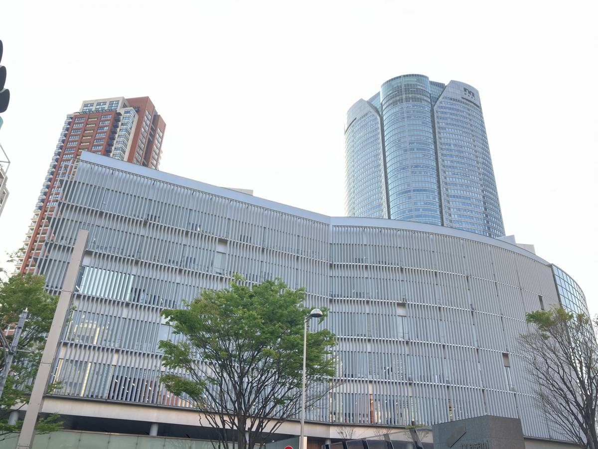 A modern curved building with a slatted facade, and two skyscrapers (one glass, one reddish-brown) behind it.