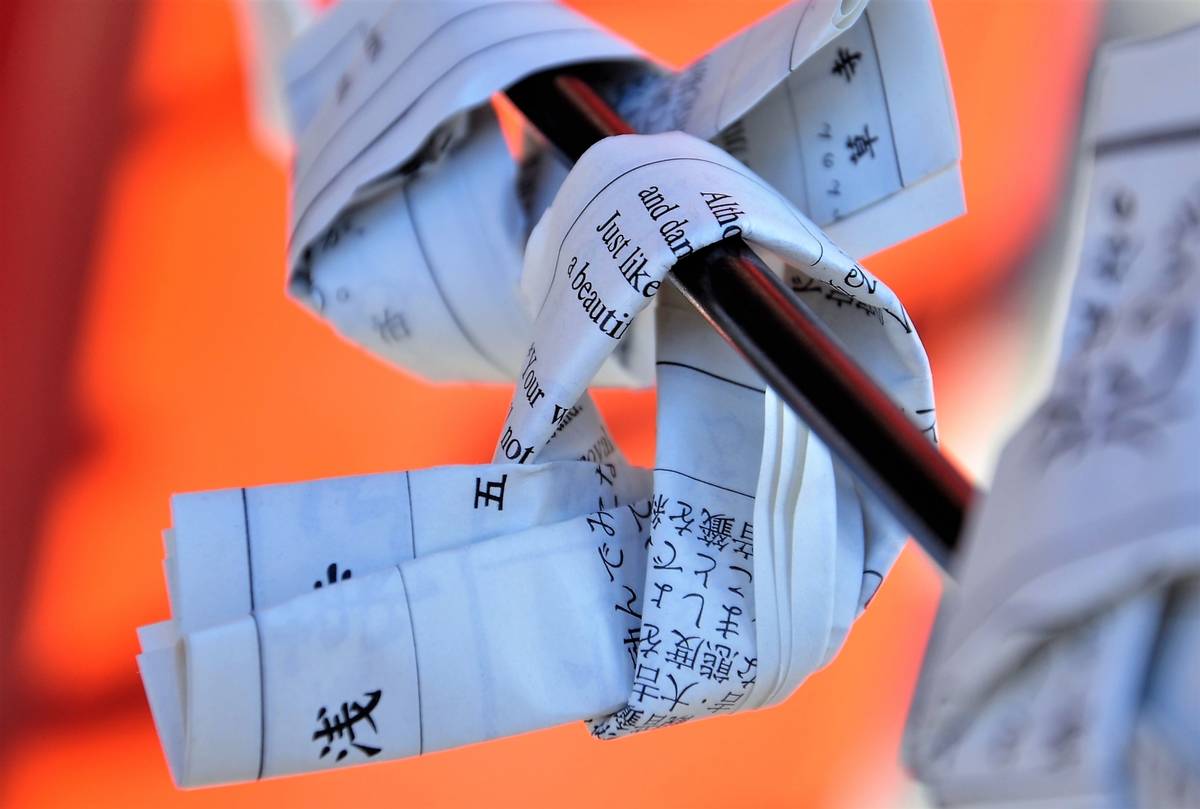 White fortune slips with text tied around a dark rod, against a blurred orange background.