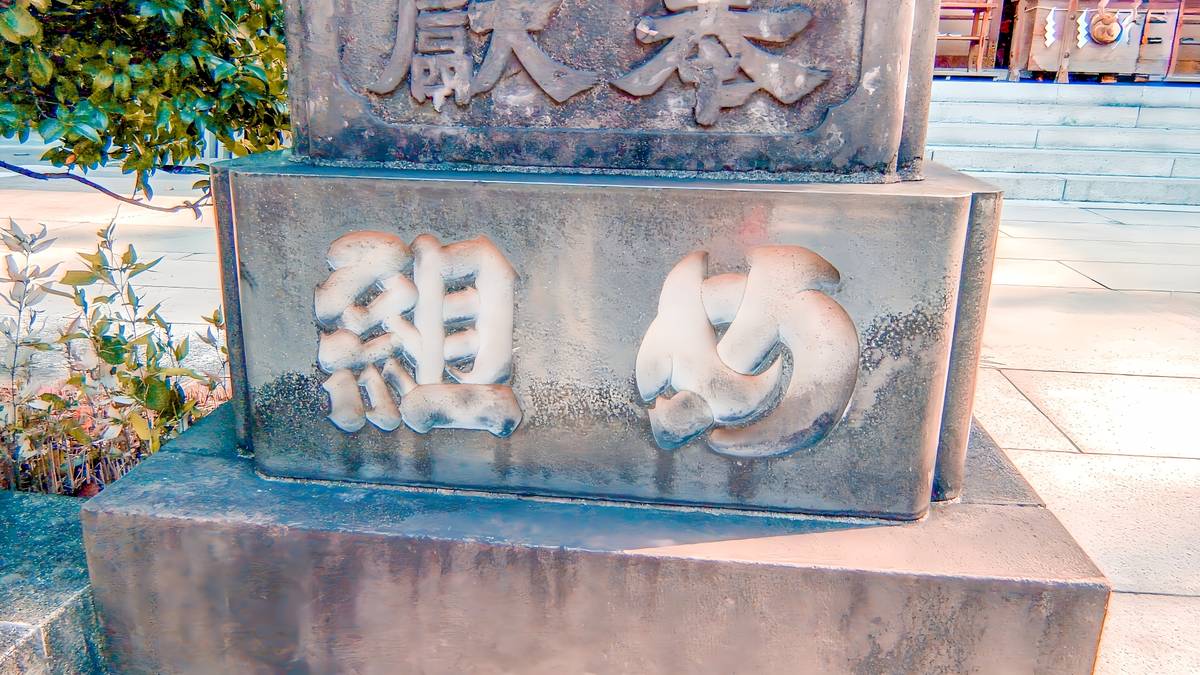Close-up of a weathered stone monument with the carved kanji character '組' and an intertwined circular emblem.
