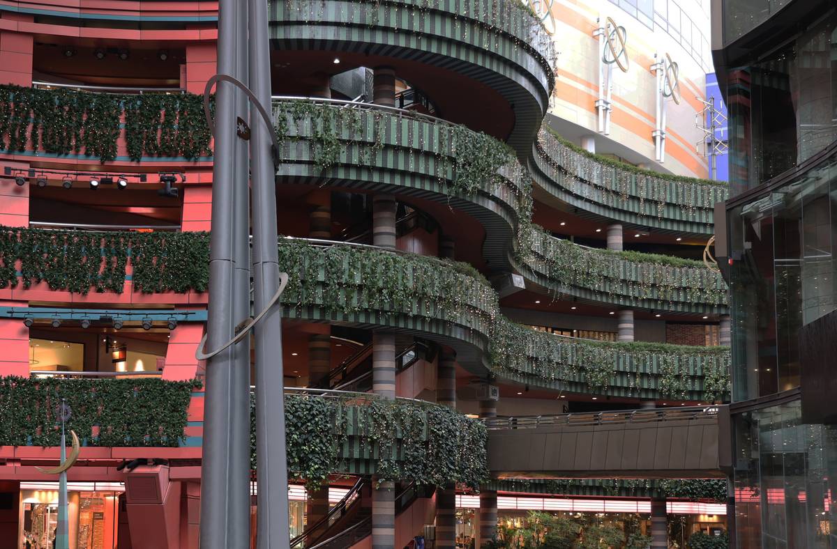 Modern building atrium with curving, vine-covered balconies and red walls.
