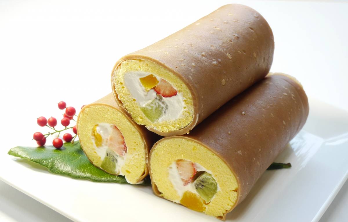 Three roll cakes, two sliced to reveal cream, strawberries, kiwi, and mango filling
