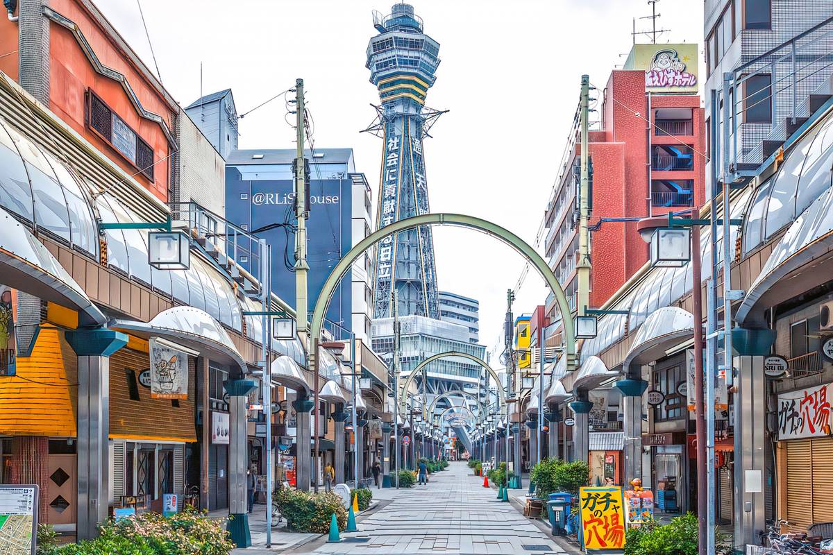 A Japanese shopping street with covered awnings leading to Tsutenkaku Tower in the distance.