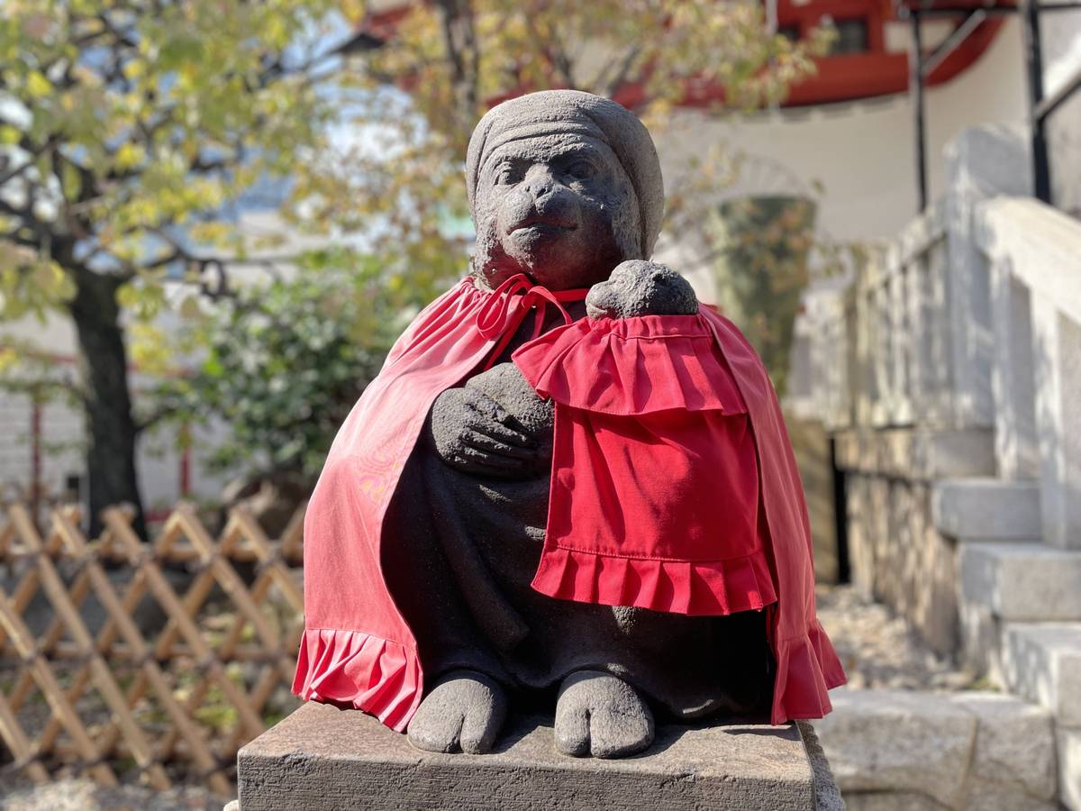 Stone monkey statue in a red cape holding a small stone figure.