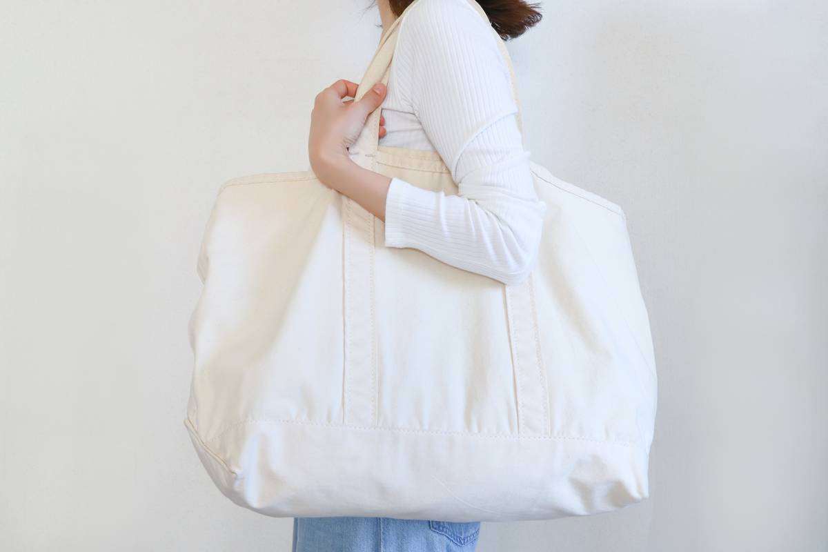 Person holding a large, natural canvas tote bag.