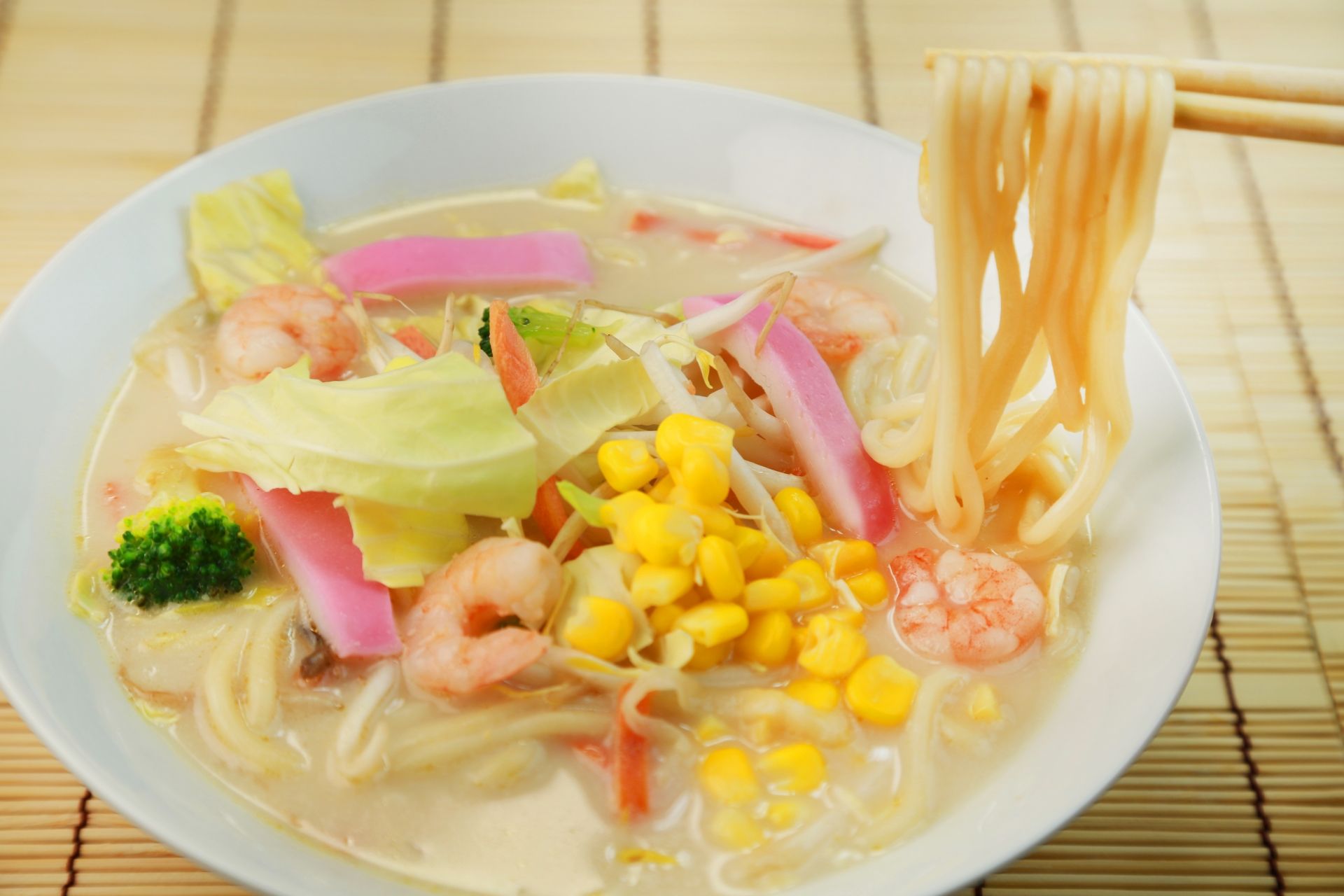 A bowl of Champon noodle soup with shrimp, corn, cabbage, broccoli, pink fish cake, and bean sprouts