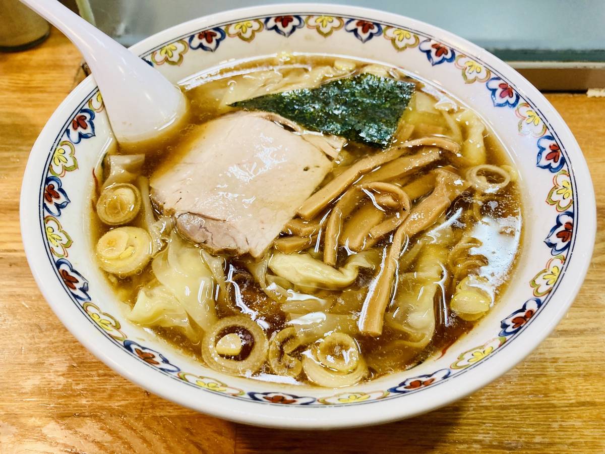 A decorative bowl of ramen with chashu pork, bamboo shoots, seaweed, and scallions in a rich broth.