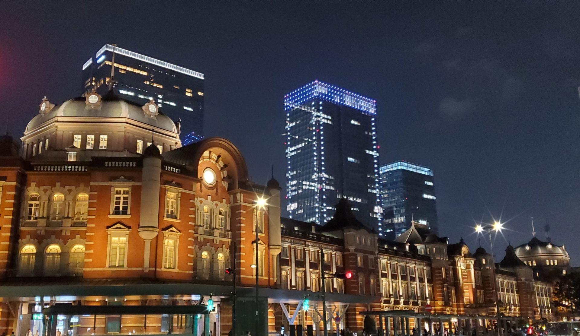 Night view of Tokyo Station's red brick facade and illuminated modern skyscrapers.