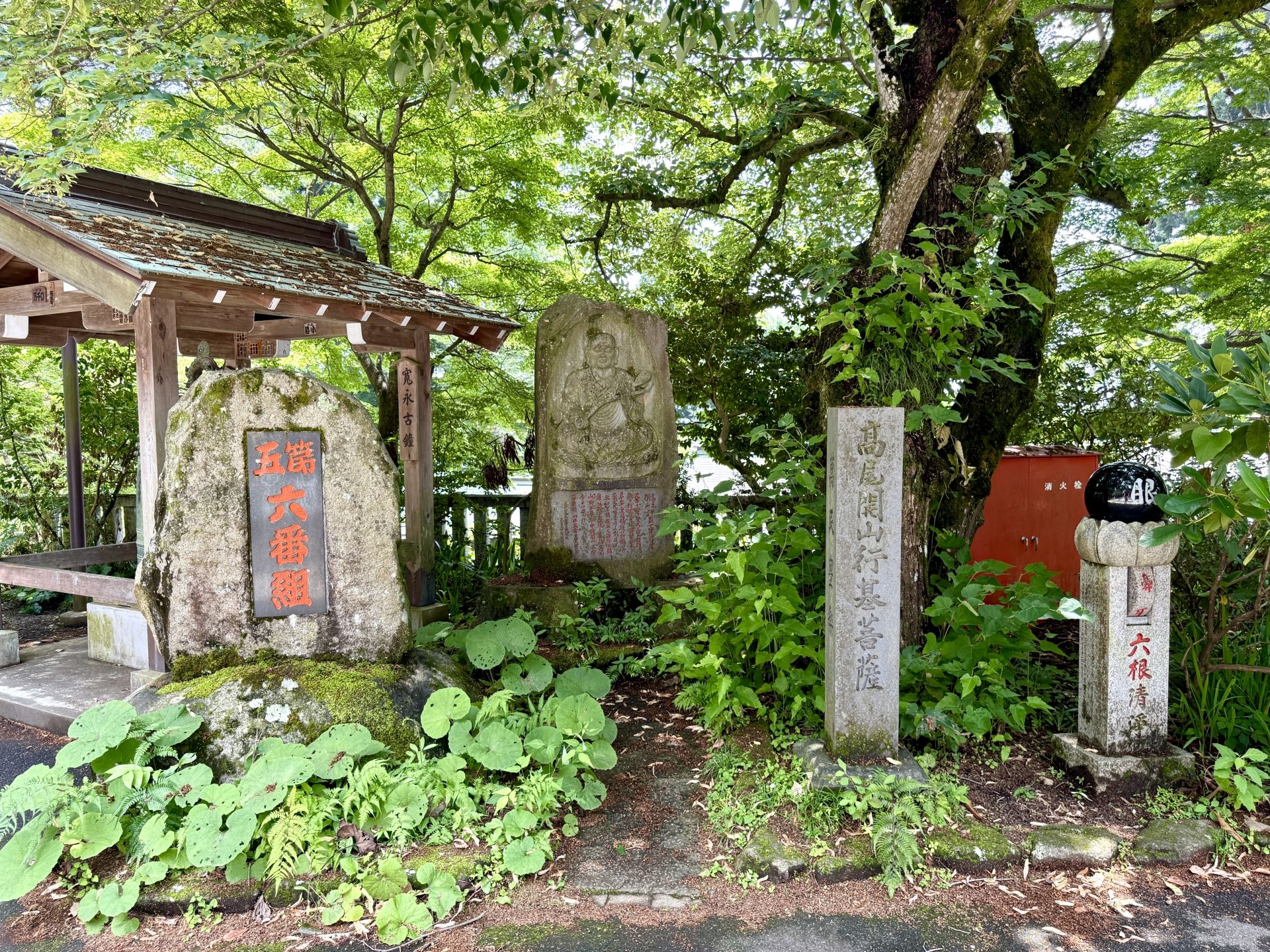 Stone monuments with Japanese inscriptions and carvings are surrounded by lush greenery and trees.