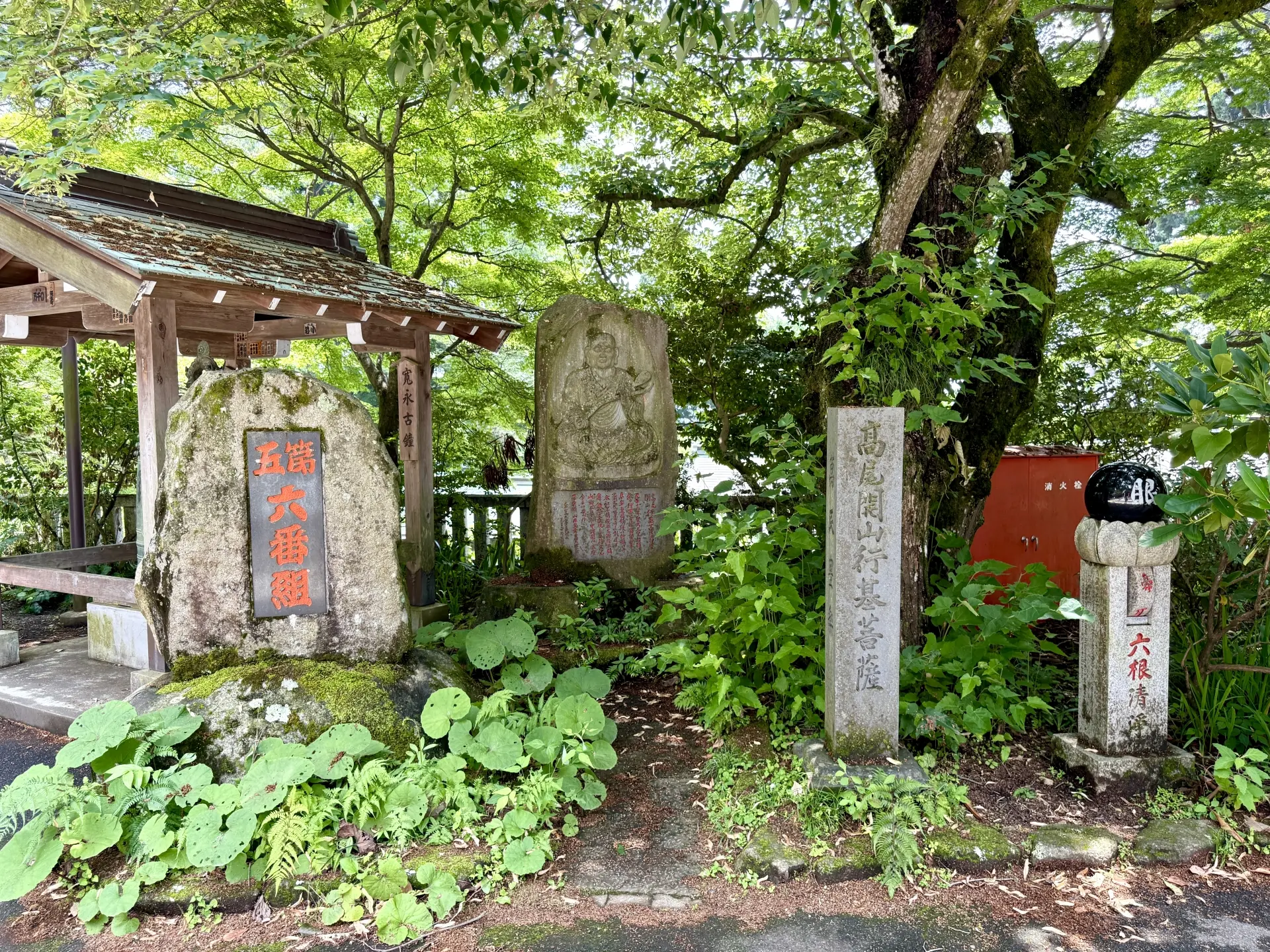 Stone monuments with Japanese inscriptions and carvings are surrounded by lush greenery and trees.