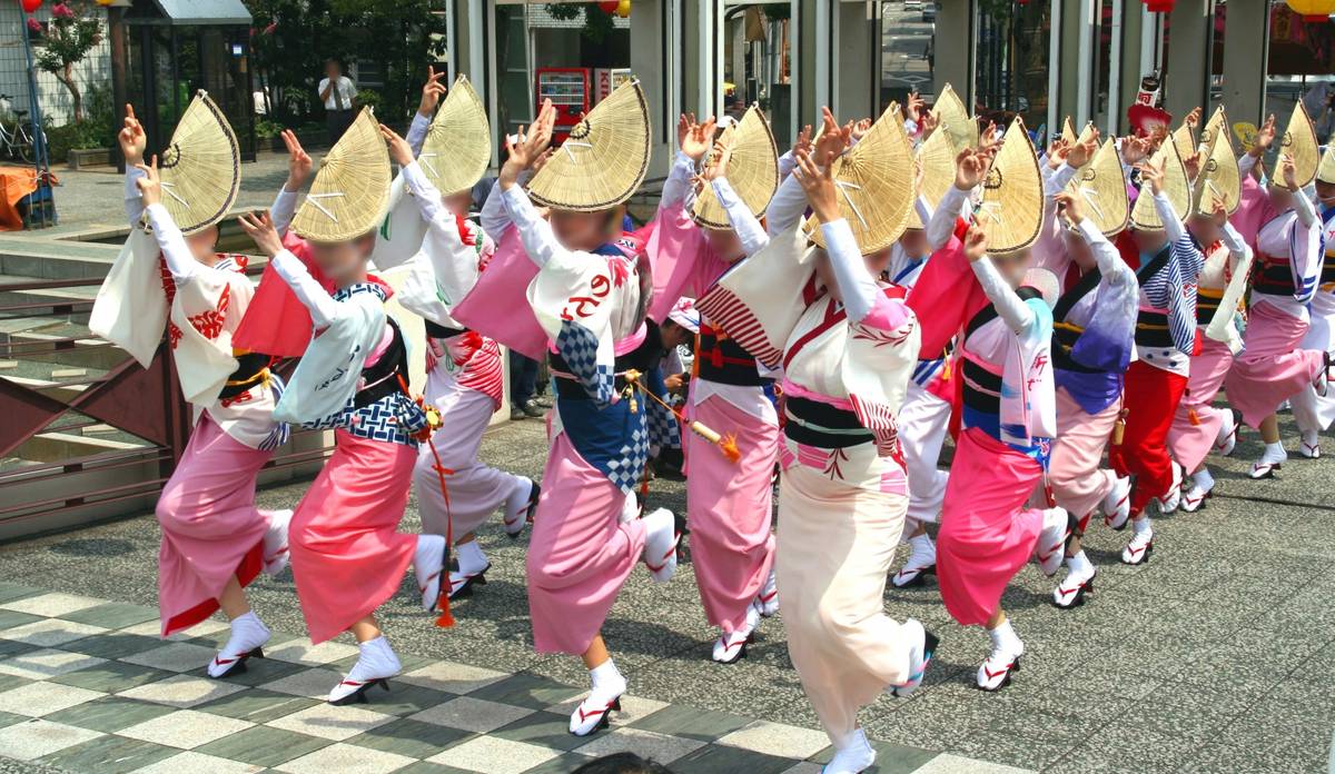 Japanese dancers in colorful kimonos and woven hats performing outdoors.