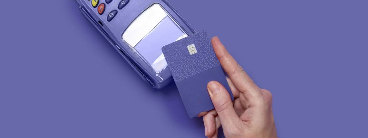 A hand holding a credit card above a payment terminal, ready for contactless payment.