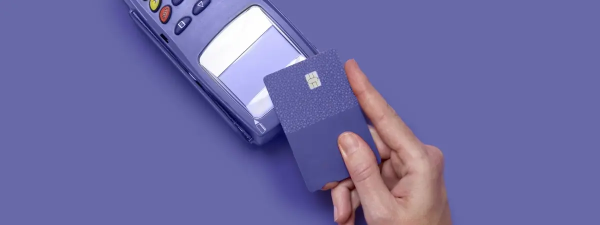 A hand holding a credit card above a payment terminal, ready for contactless payment.