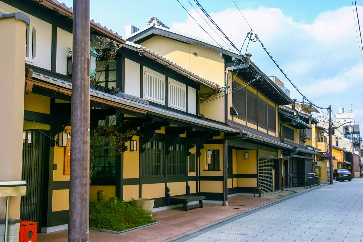 Street lined with traditional Japanese buildings with yellow walls and dark trim under a blue sky.