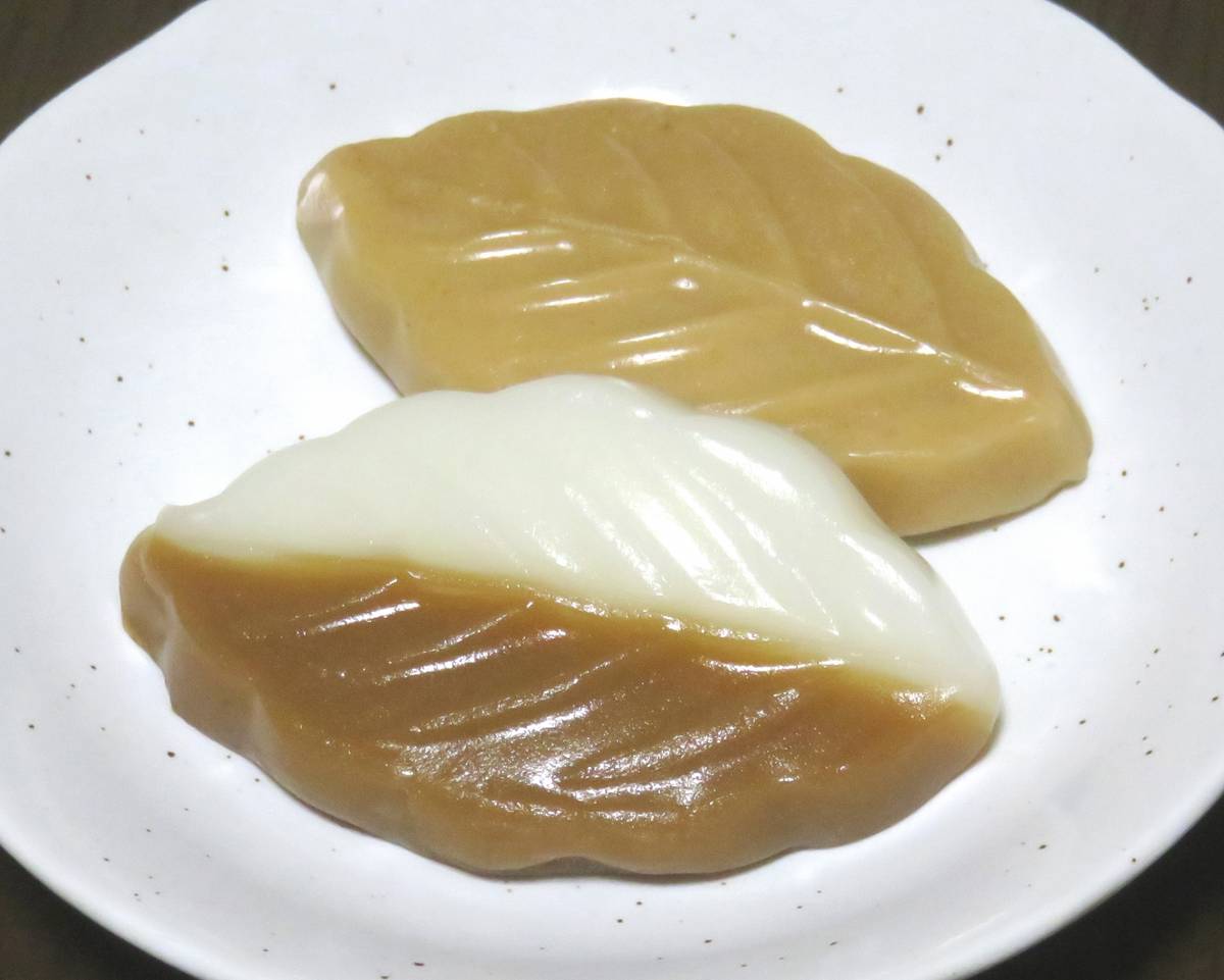 Two leaf-shaped sweets, one brown and one white and brown, on a white plate.
