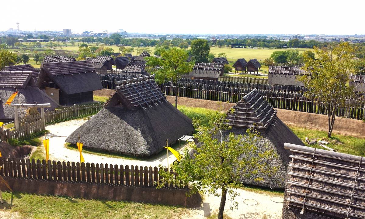 Reconstructed ancient village with multiple thatched-roof houses and wooden palisades.