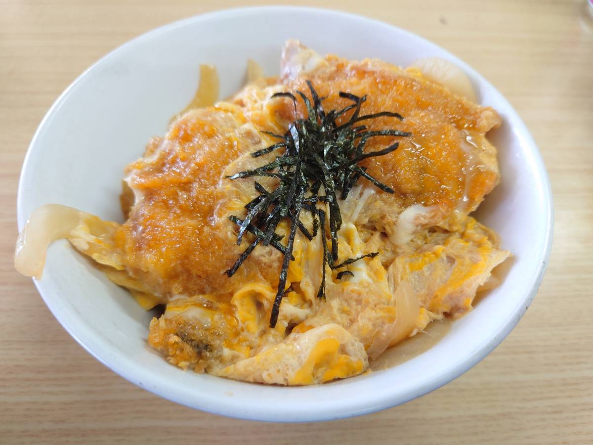 A white bowl of fried cutlet, egg, and onions, topped with shredded nori.