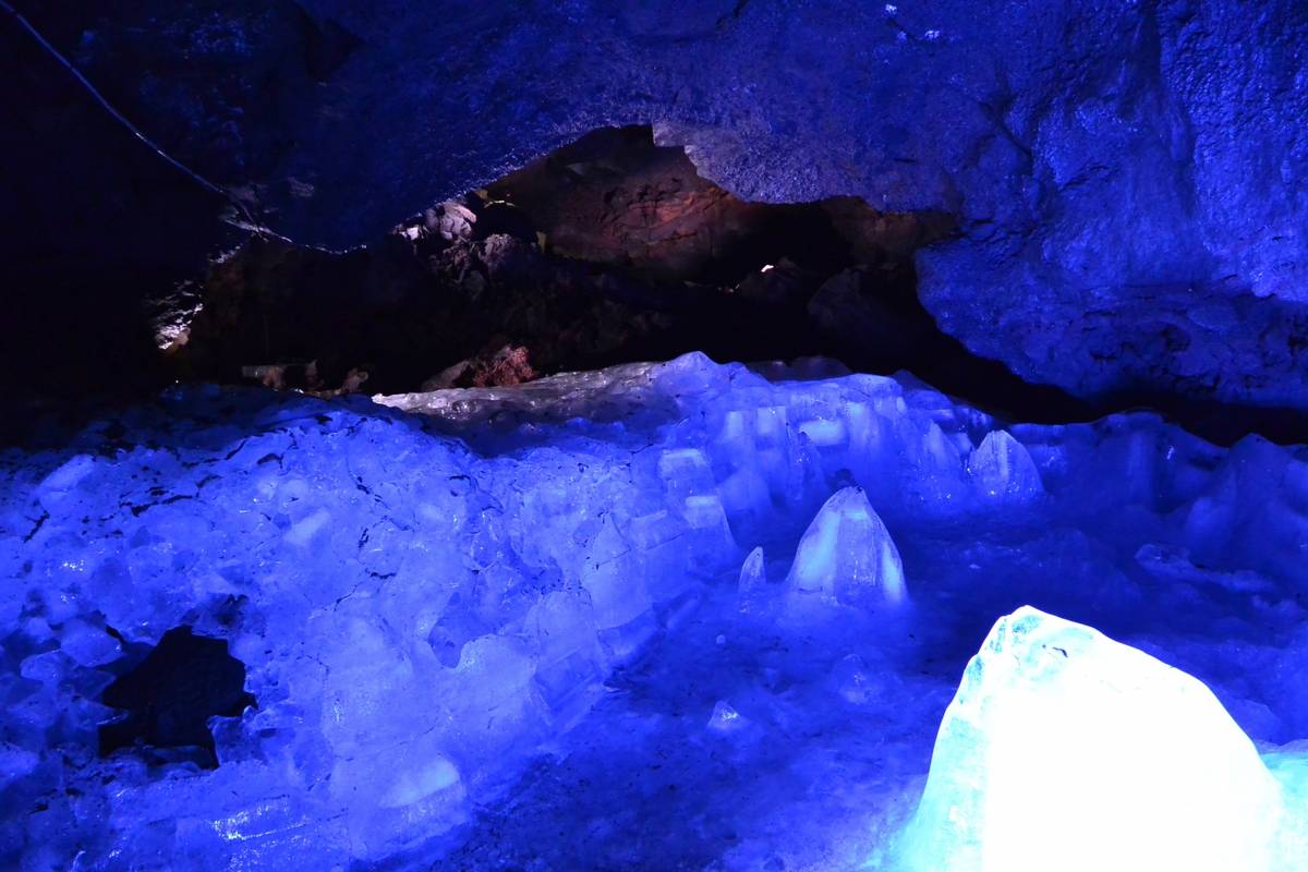 Ice formations inside a dark cave, illuminated by a vivid blue light.