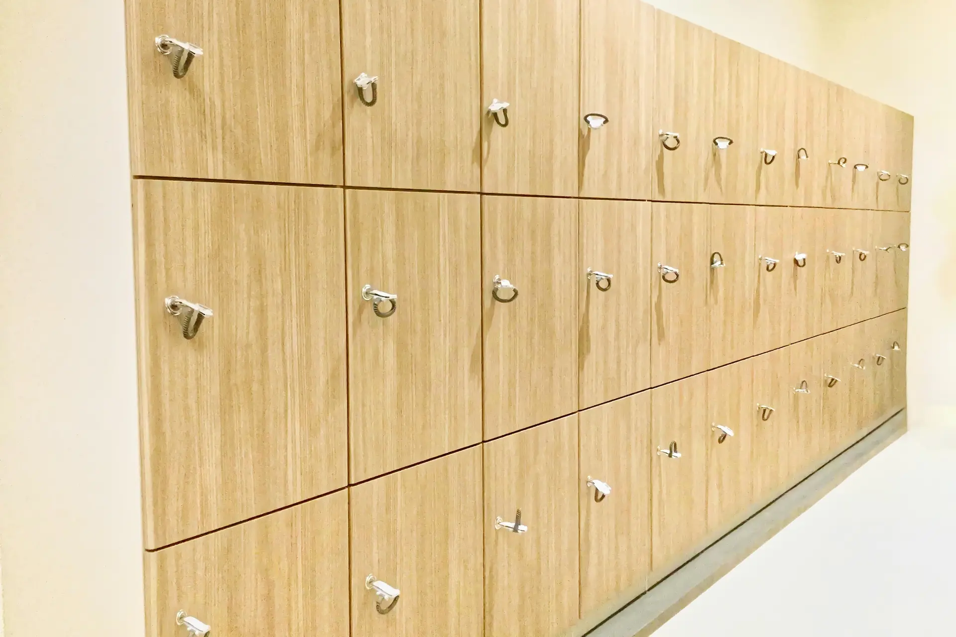A wall of modern light wood lockers with chrome handles.