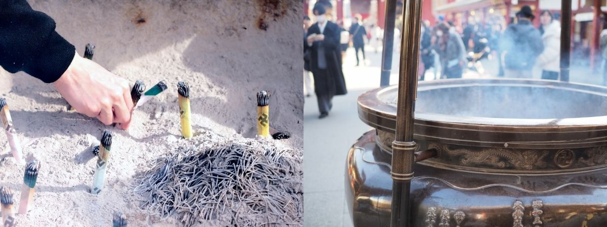 A hand places an incense stick into sand, next to a large, smoking communal incense burner at a temple.