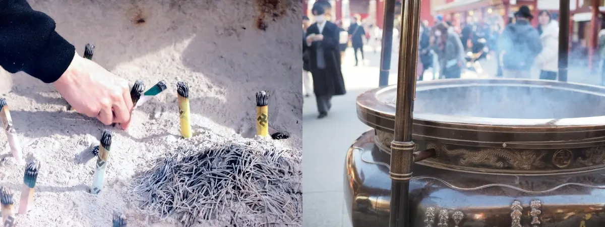 A hand places an incense stick into sand, next to a large, smoking communal incense burner at a temple.