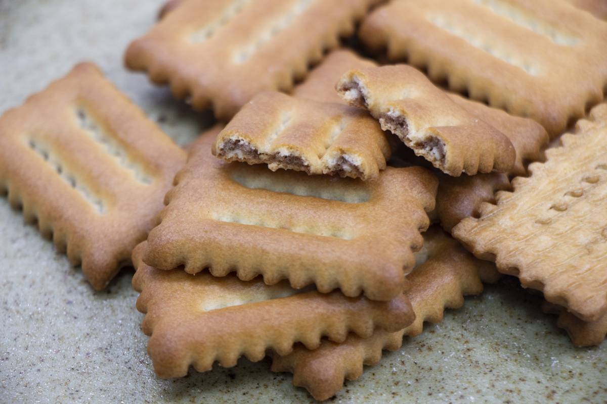 Rectangular biscuits with scalloped edges and three parallel indentations, one broken to reveal a light brown filling.