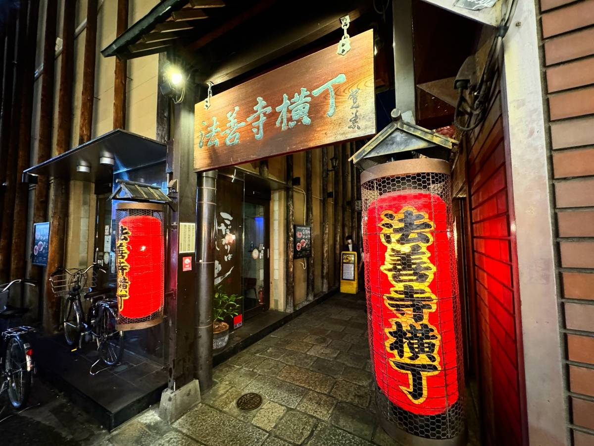 Night view of Hozenji Yokocho alley in Japan, with red lanterns and a wooden sign.