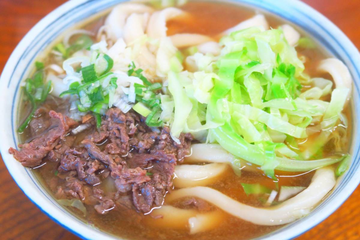 A bowl of udon noodles with beef, cabbage, and green onions in broth.
