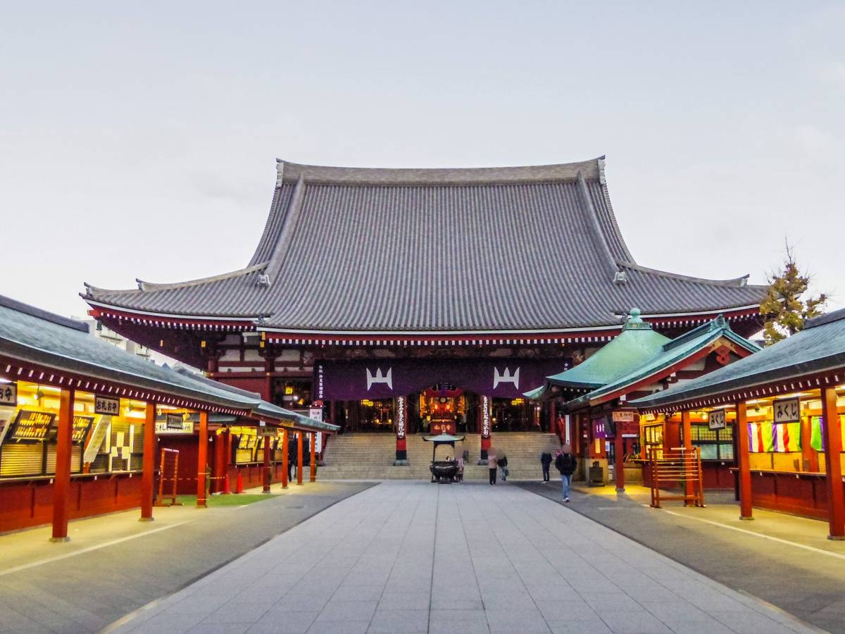 A traditional Japanese temple seen from a pathway lined with small, illuminated shops.
