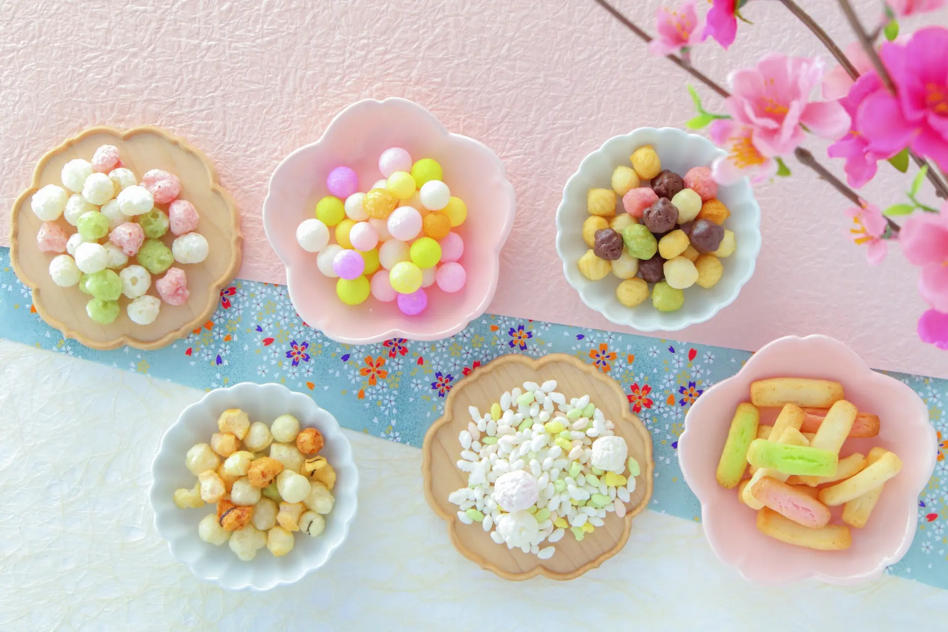 An assortment of pastel Japanese sweets in various bowls, with cherry blossoms.