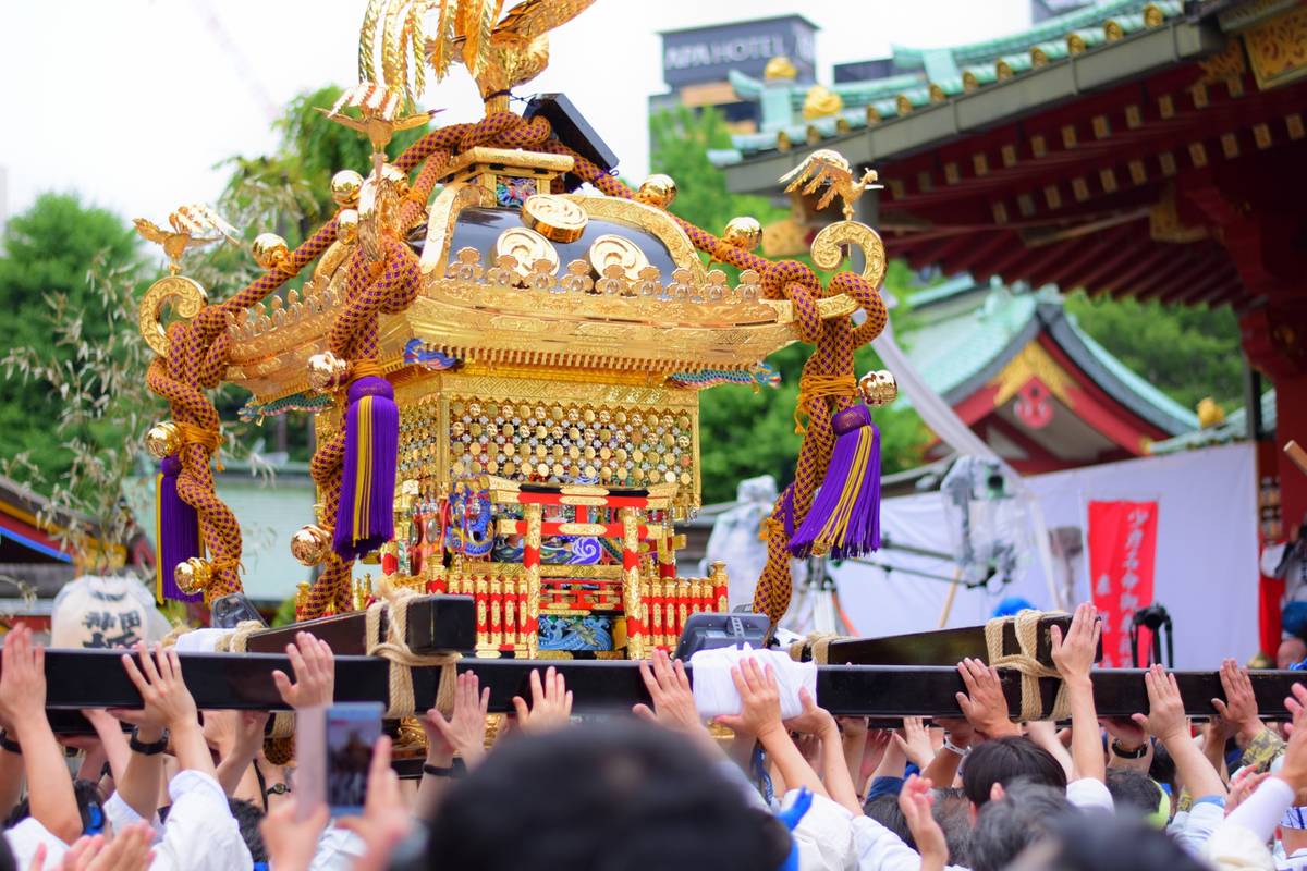 Ornate golden mikoshi being carried by many people in a procession.