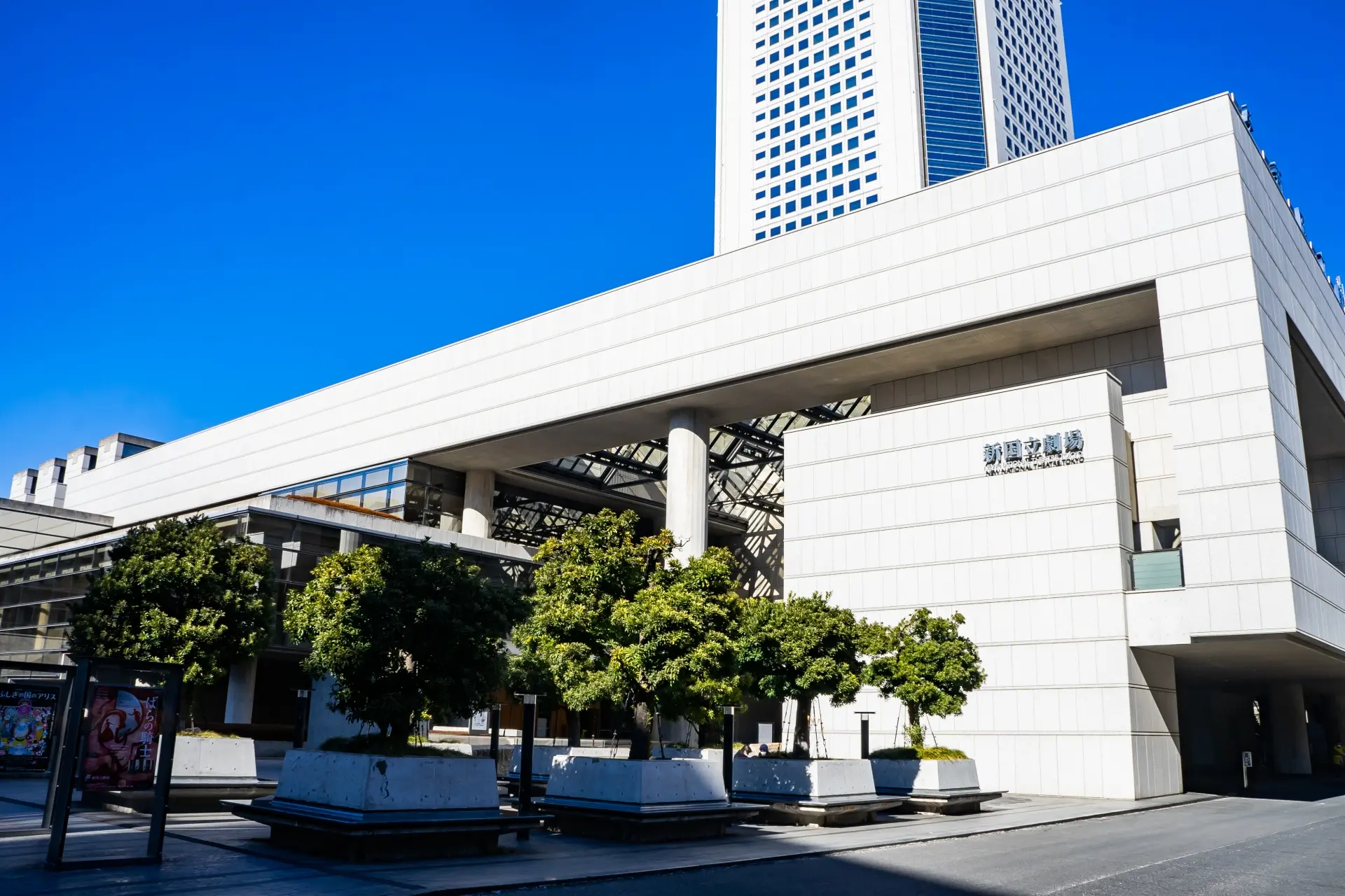 Exterior of the New National Theatre, Tokyo, a modern white building with trees in front and a skyscraper behind