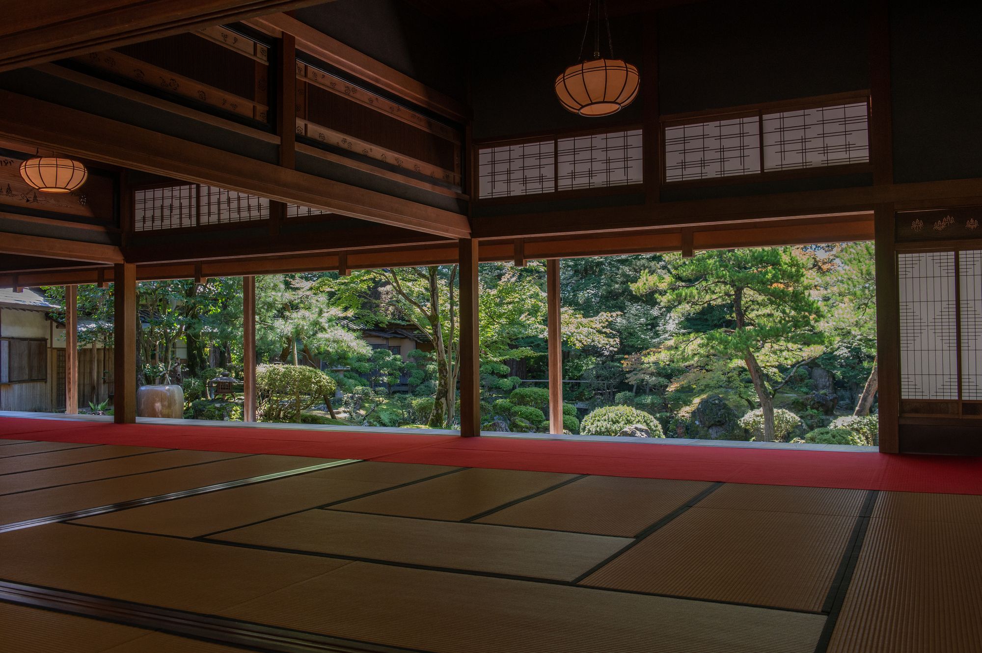 A traditional Japanese room with tatami floor and a red walkway, looking out onto a vibrant garden.