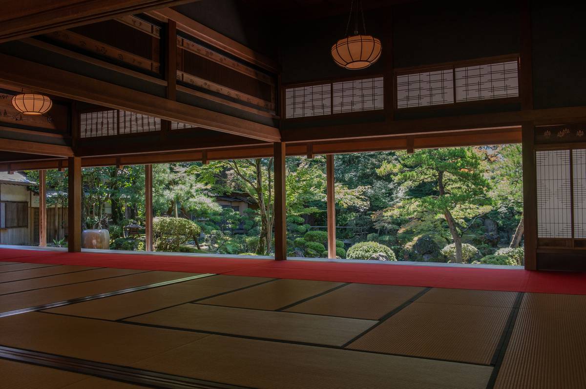 A traditional Japanese room with tatami mats and a red border, opening to a lush garden.