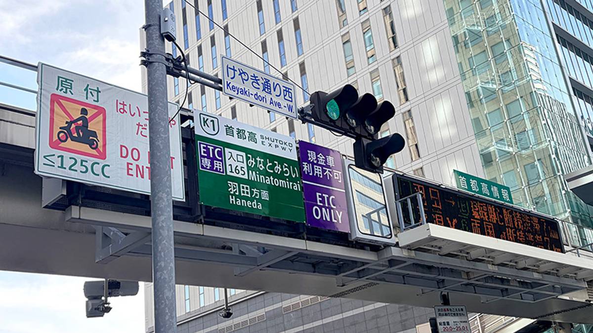 Overhead road signs and a green traffic light in front of a modern building. Signs warn motorcycles to 'DO NOT ENTER' and show expressway directions with 'ETC ONLY' payment details.