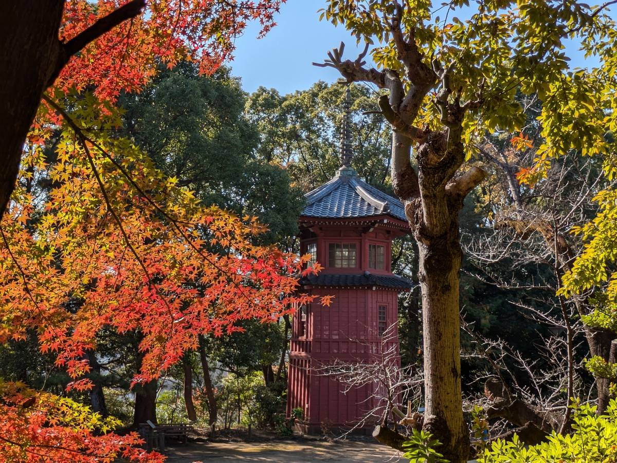 A red hexagonal building stands among brilliant autumn foliage under a blue sky.