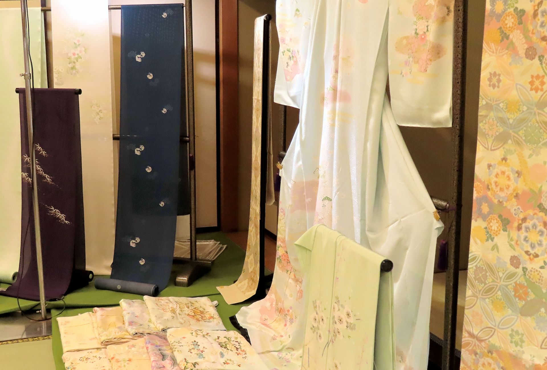 Display of various patterned Japanese fabrics, including rolls, draped cloths, and folded pieces.