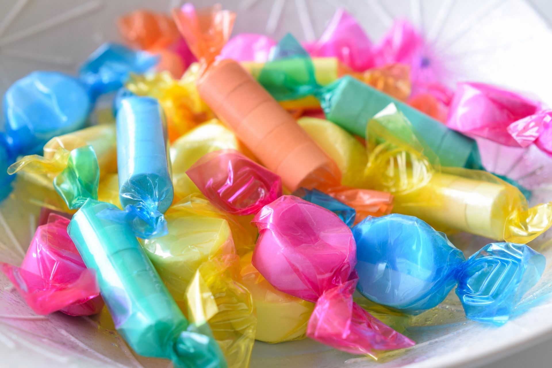 A white bowl filled with assorted candies in pink, blue, yellow, green, and orange translucent wrappers.