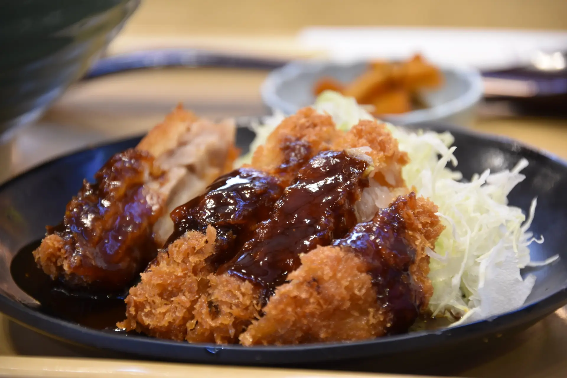 Crispy breaded cutlets with dark sauce and shredded cabbage on a black plate.