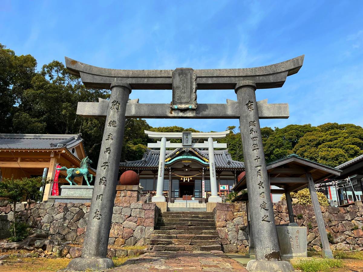 A stone torii gate stands before a traditional Japanese shrine reached by stone steps 