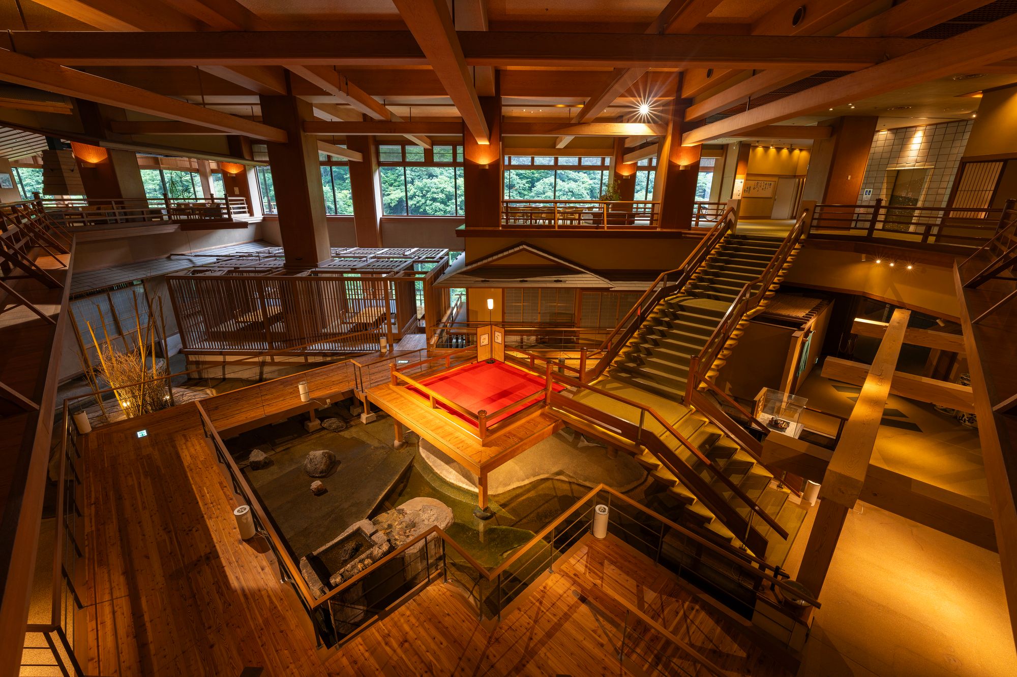 A multi-level interior with extensive wooden architecture, a grand central staircase, and indoor water features.