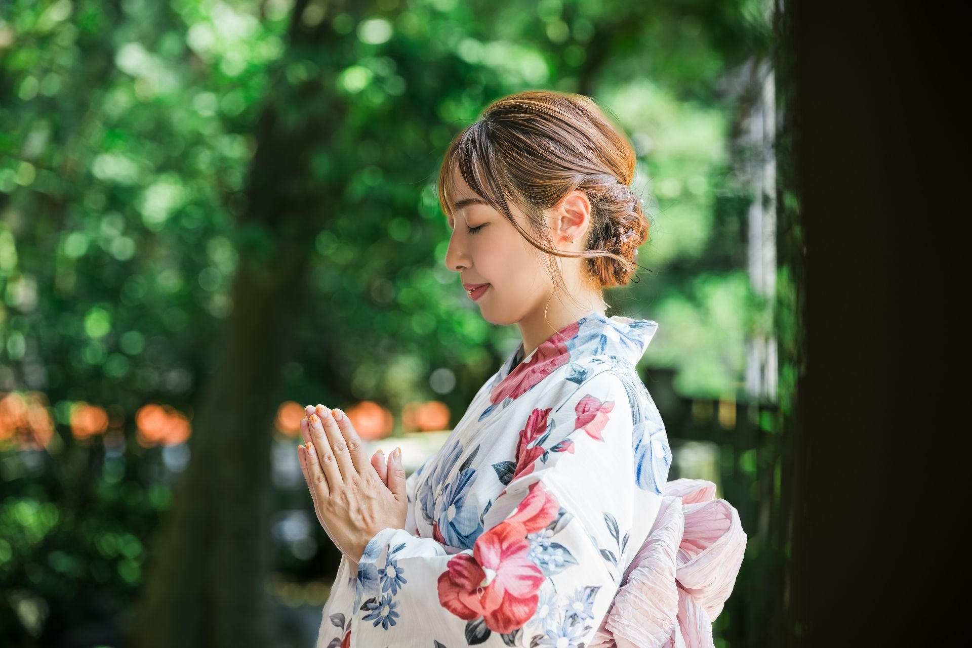 Woman in floral yukata with hands pressed together in prayer, eyes closed.