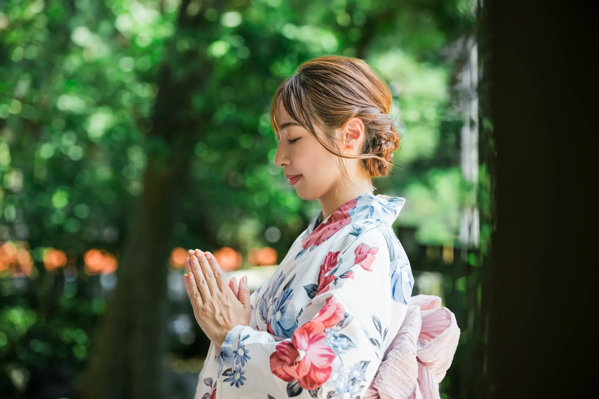 Woman in floral yukata with hands pressed together in prayer, eyes closed.