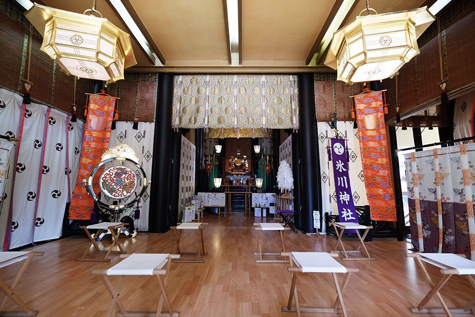 Interior of Hikawa Shinto Shrine with an altar, large lanterns, banners, a drum, and small stools.