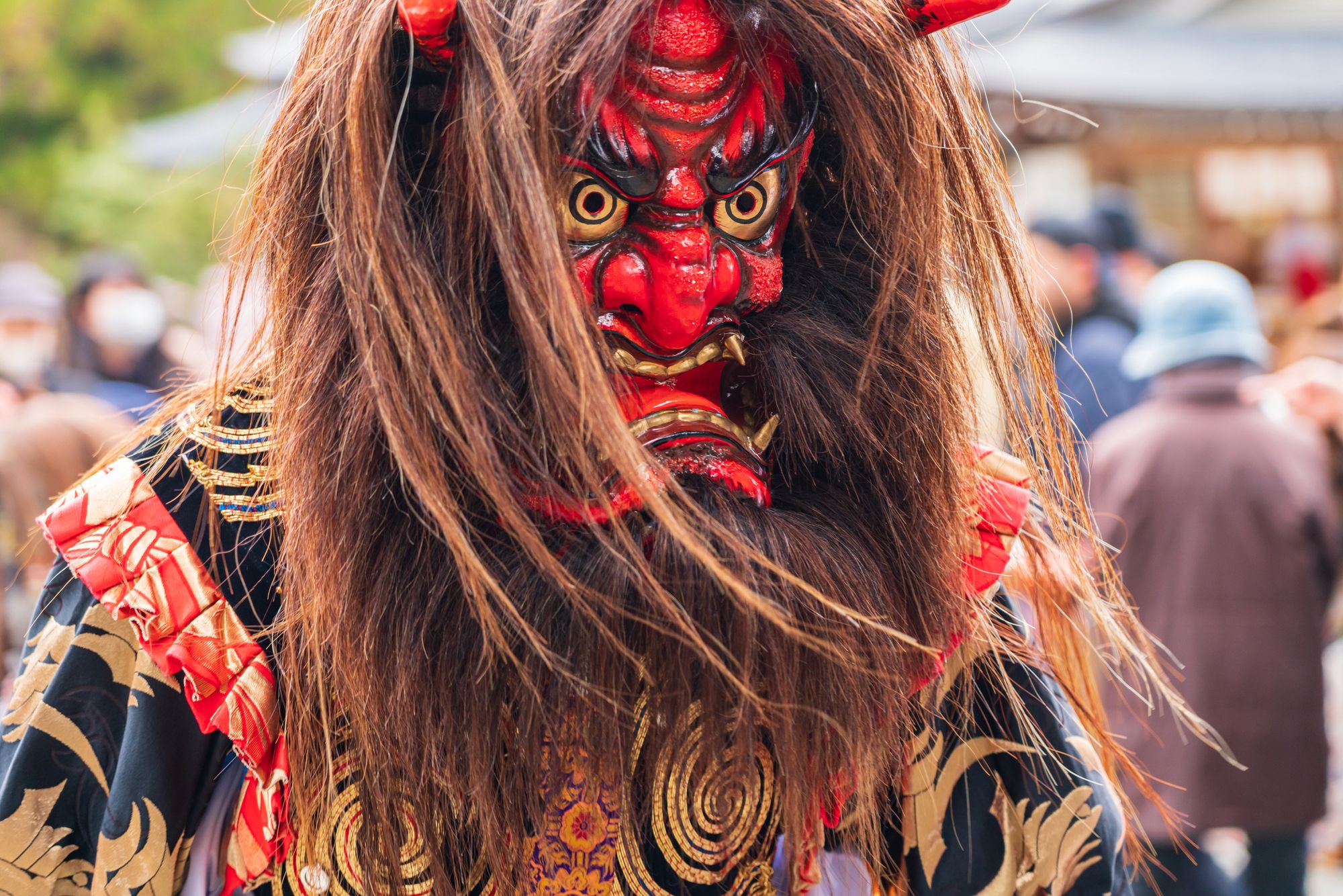 Person wearing a vibrant red Japanese Oni mask with golden eyes, long hair, and an ornate costume.