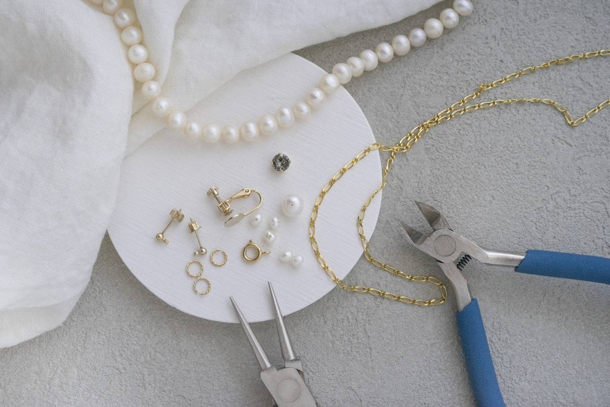 Jewelry making supplies including a pearl necklace, gold chain, various findings, beads, and pliers.