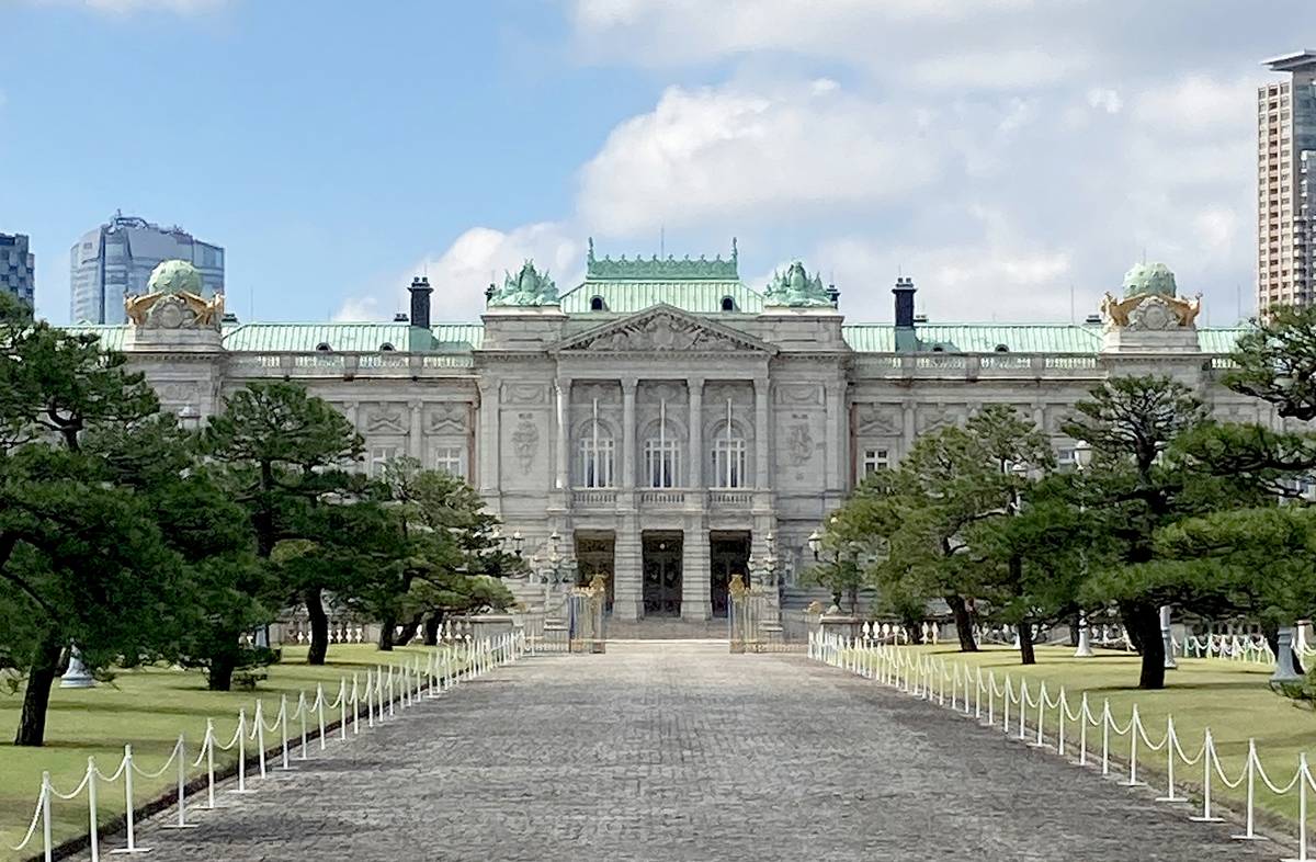 Grand white palace with a green roof, formal gardens, and a paved entrance.