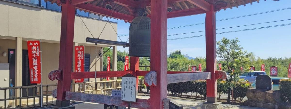 Bronze temple bell inside a red wooden bell tower, with red banners in the background.