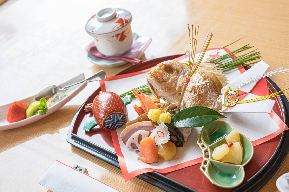 An elaborate traditional Japanese meal with a whole fish, shrimp, and various colorful dishes artfully arranged on a black tray.